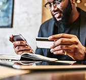 Man with glasses, holding cellphone looking at credit card