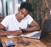 Man sitting at laptop with calculator, writing out financial goals