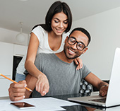 Man and woman smiling, looking at paperwork and laptop