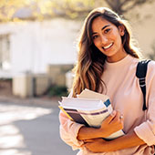 College student standing and smiling holding a stack of books