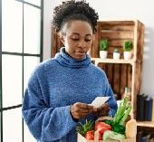 Woman looking at her phone, calculating savings with a bag of groceries