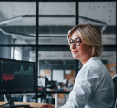 Woman sitting at desk, looking at stocks on computer screen.