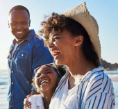 Family of 3 smiling and laughing together on the beach.