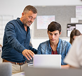 Professor standing next to college student providing instruction. 