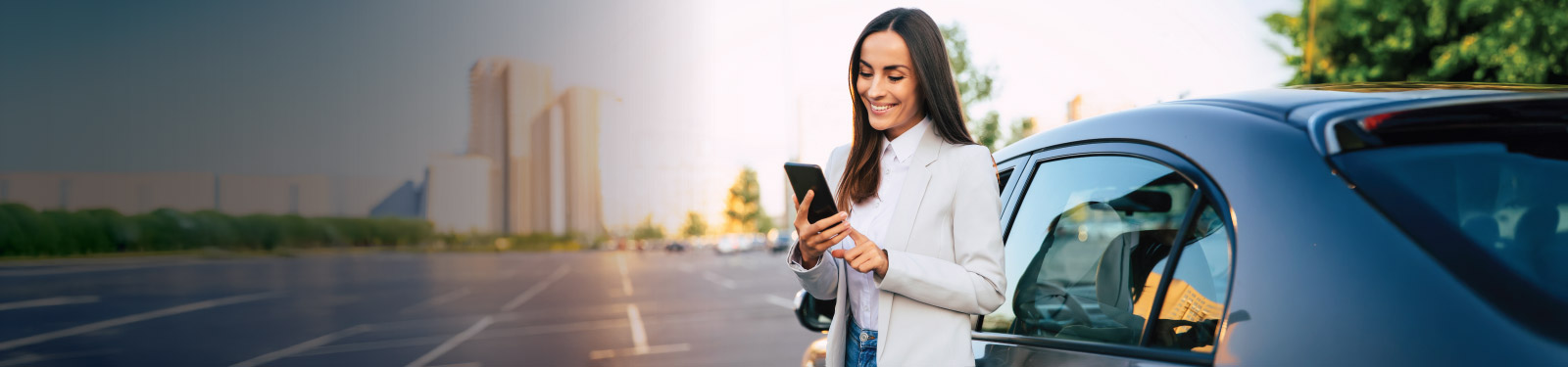 Woman leaning against her car and smiling at something on her phone